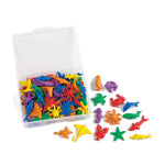 A clear plastic storage box filled with small colorful sea creature toy pieces, with several loose toy pieces arranged beside it on a white background.