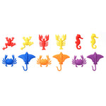 A set of plastic aquatic counters arranged in two rows on a plain white background to show color patterning. First line of like red frog, yellow frog, red lobster, yellow lobster, red seahorse, yellow seahorse. Second line of blue crab, blue ray, orange crab, orange ray, purple crab, and purple ray.